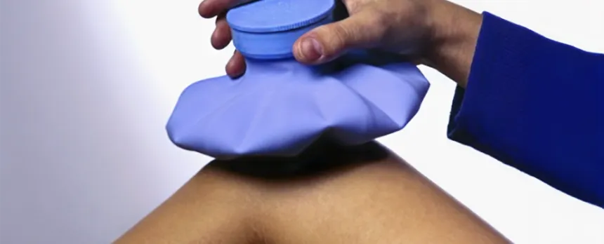 Someone's hand is holding a blue ice bag in place on their bent knee.