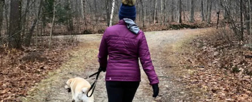woman walking dog down trail in woods