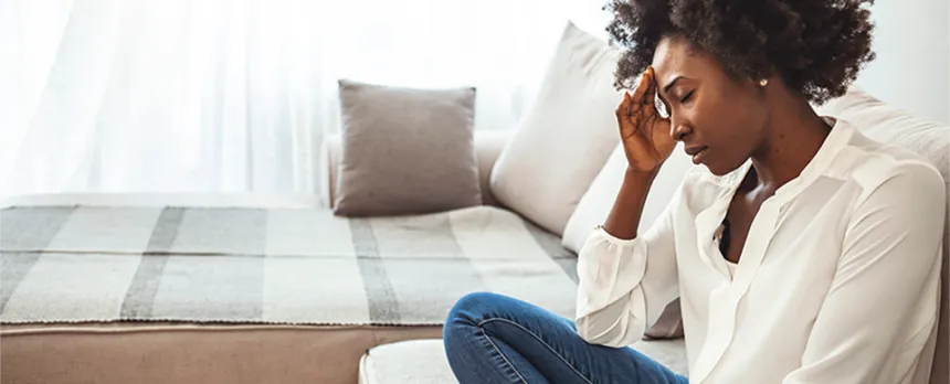 I black woman sitting cross-legged in a chair, hand on forehead and eyes closed.