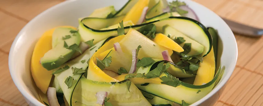 A white bowl is full of yellow and green zucchini noodles.