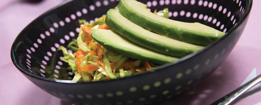 A black bowl with a salad topped with avocado.