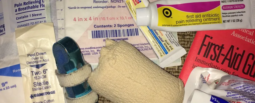 A closeup shows various medical supplies in a first aid kit, including gauze, ointments, and bandages.