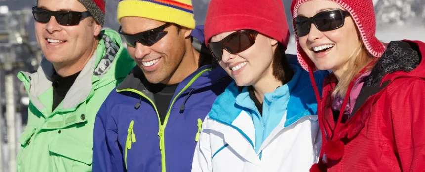 A group of young adults are wearing sunglasses and winter clothes while smiling on a snowy mountain.