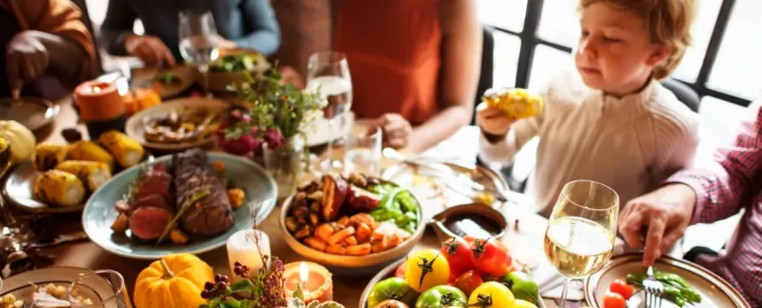 A child sits at a table full of food and people.