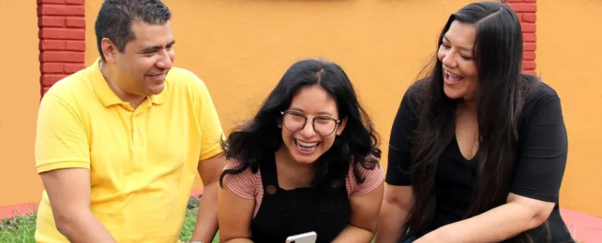 A mother, father, and daughter are sitting on a ledge, laughing together.
