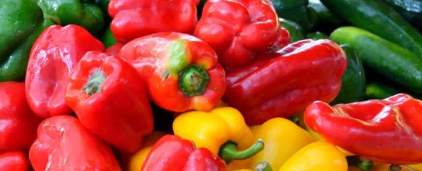Red and yellow peppers are on a pile of other vegetables.