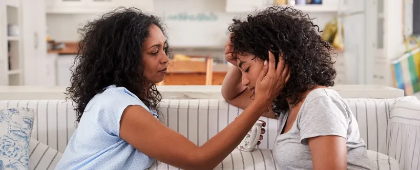 A woman is comforting a teenager on a couch.