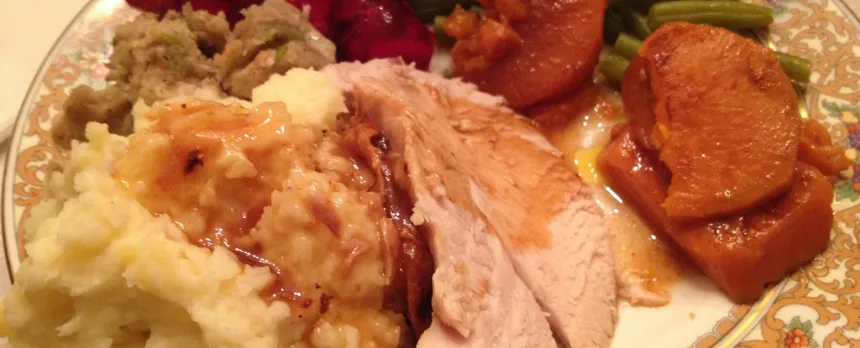 A closeup of a Thanksgiving dinner with turkey, masked potatoes, stuffing, and vegetables.