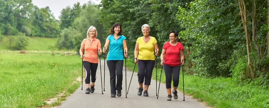 A group of mature women with hiking sticks are walking on a path.