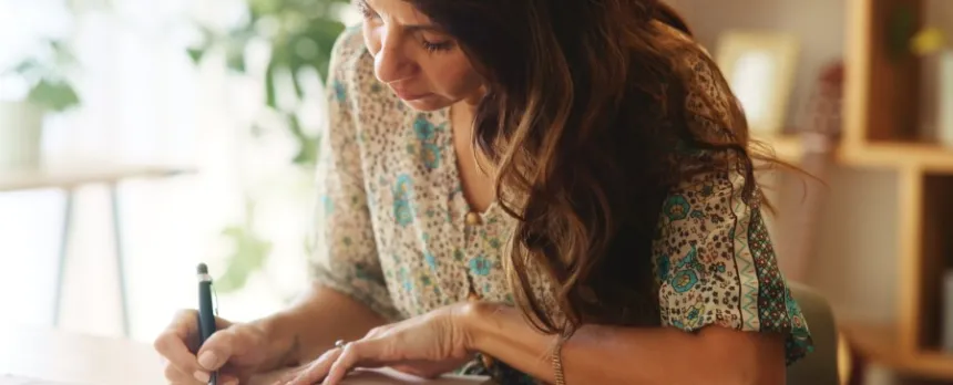 A woman sits at a desk, conducting research and taking notes.