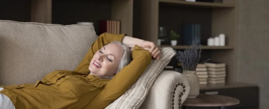 A woman in a yellow shirt is laying on a couch with her arms above her head.