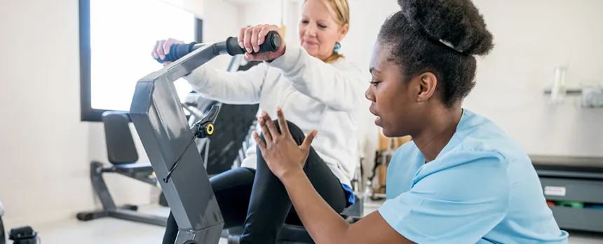 A nurse helps a patient on an exercise machine as part of her rehabilitation therapy.